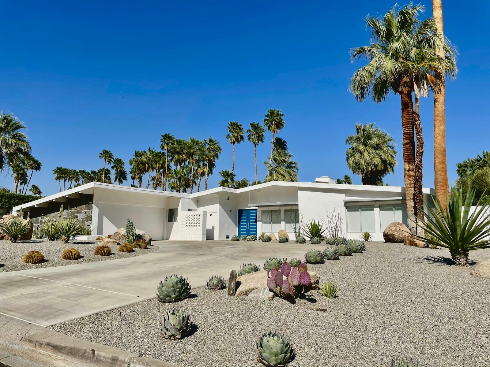 White mid-century modern California home with palm trees and a clear blue sky