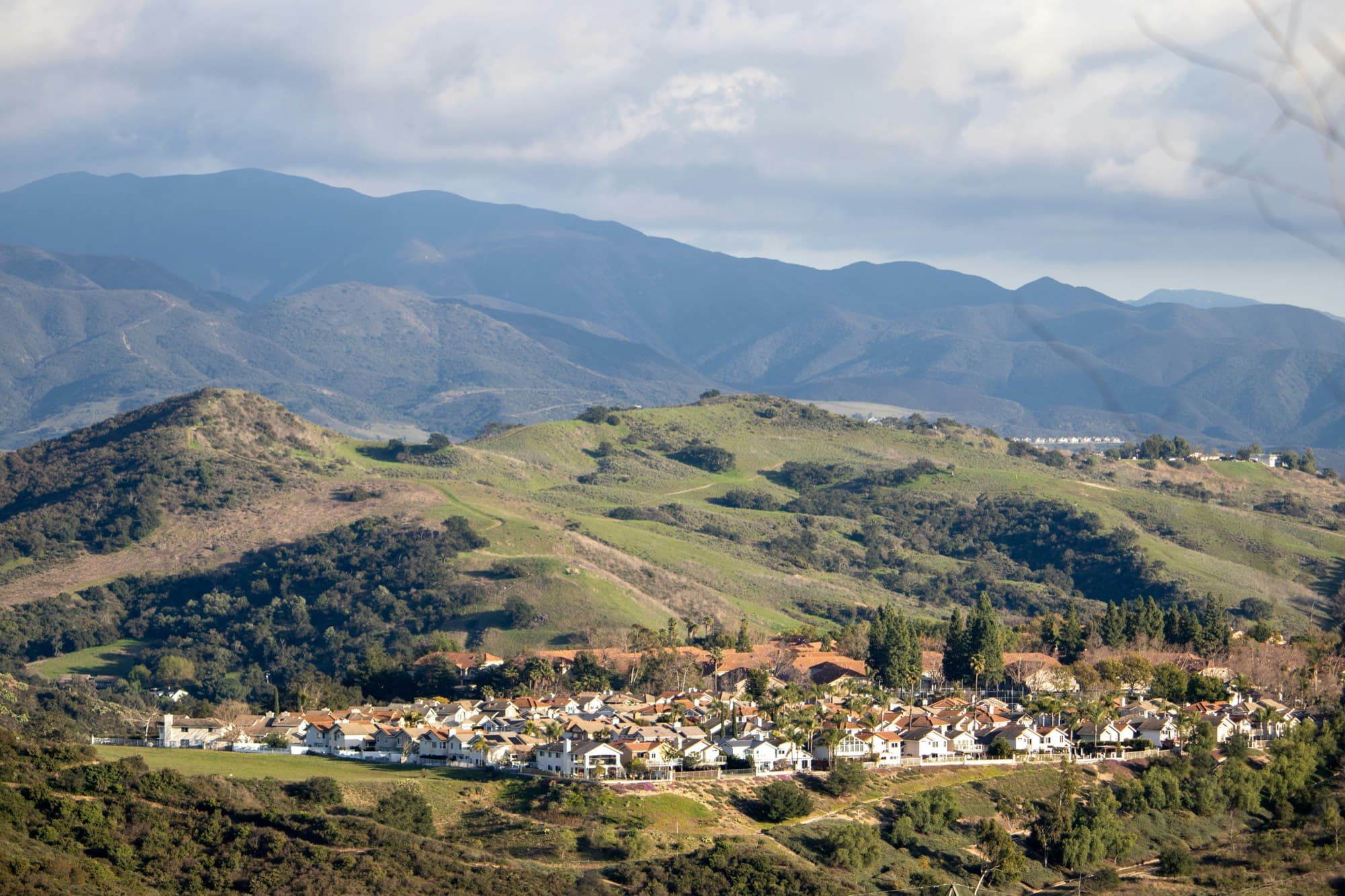 Rancho Santa Margarita neighborhood of tile-roofed homes below green oak-dotted foothills, with the Santa Ana Mountains behind