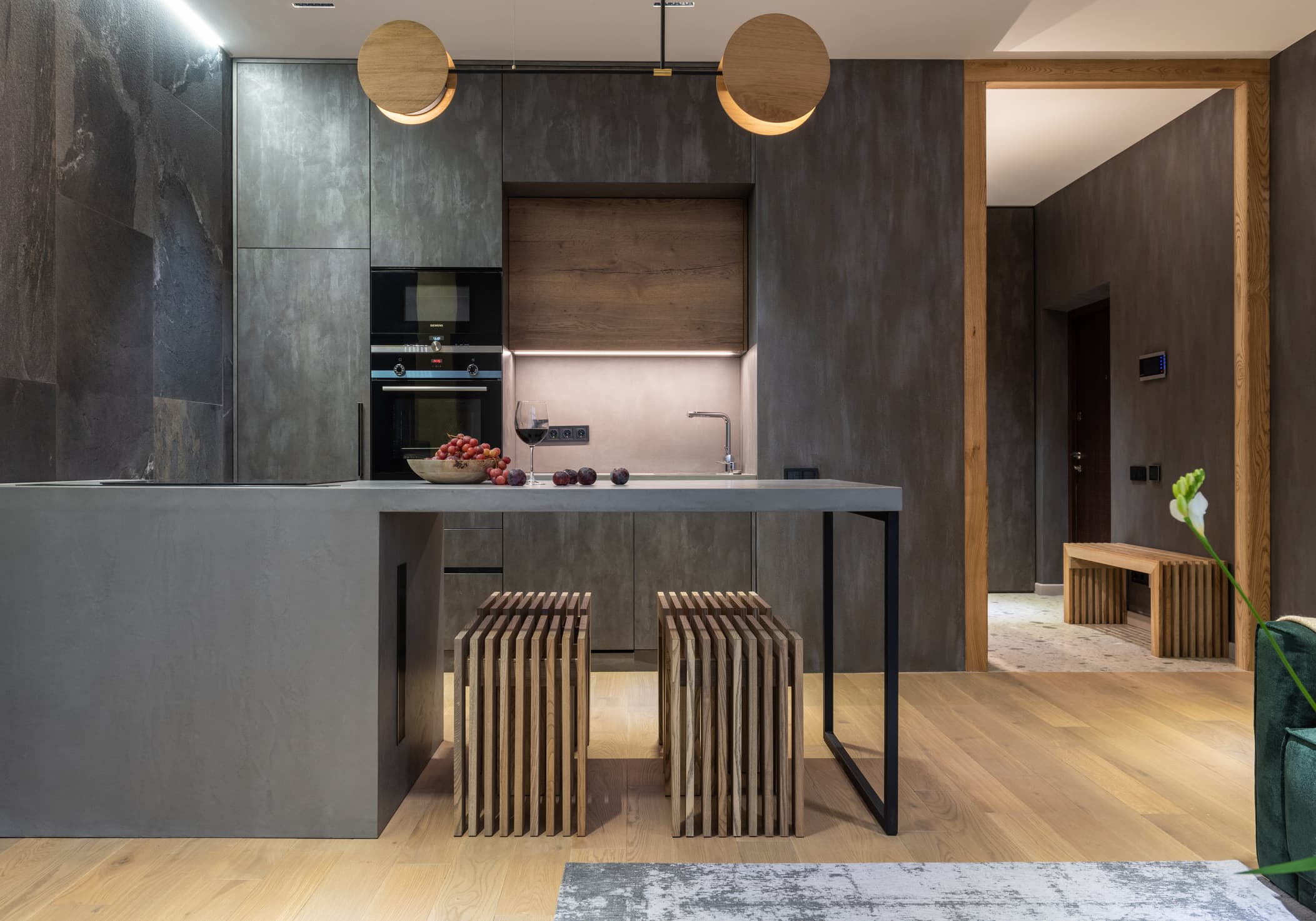 Dark, dramatic modern kitchen with concrete island, slat-wood stools, and pendant lighting